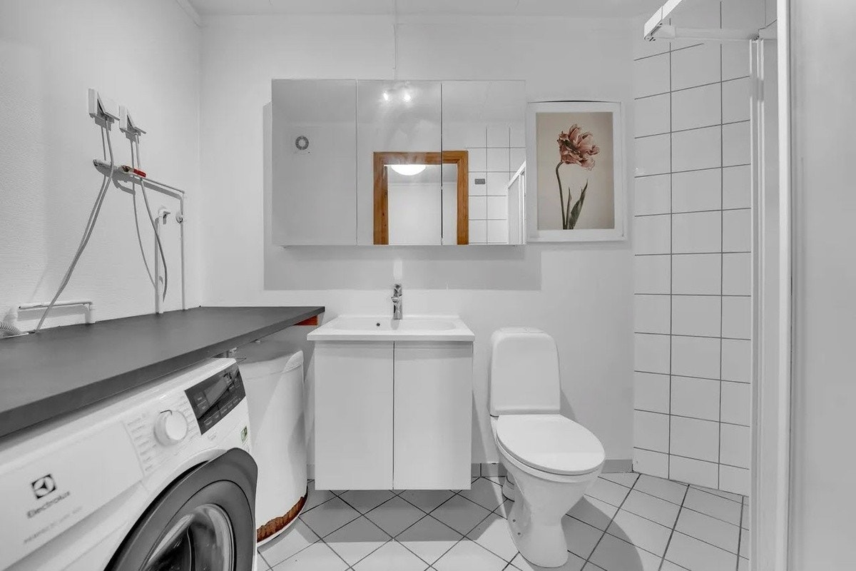 Badet er innredet med gulvmontert toalett, servant med underskap, dusjhjørne og opplegg for vaskemaskin. Galleribilde