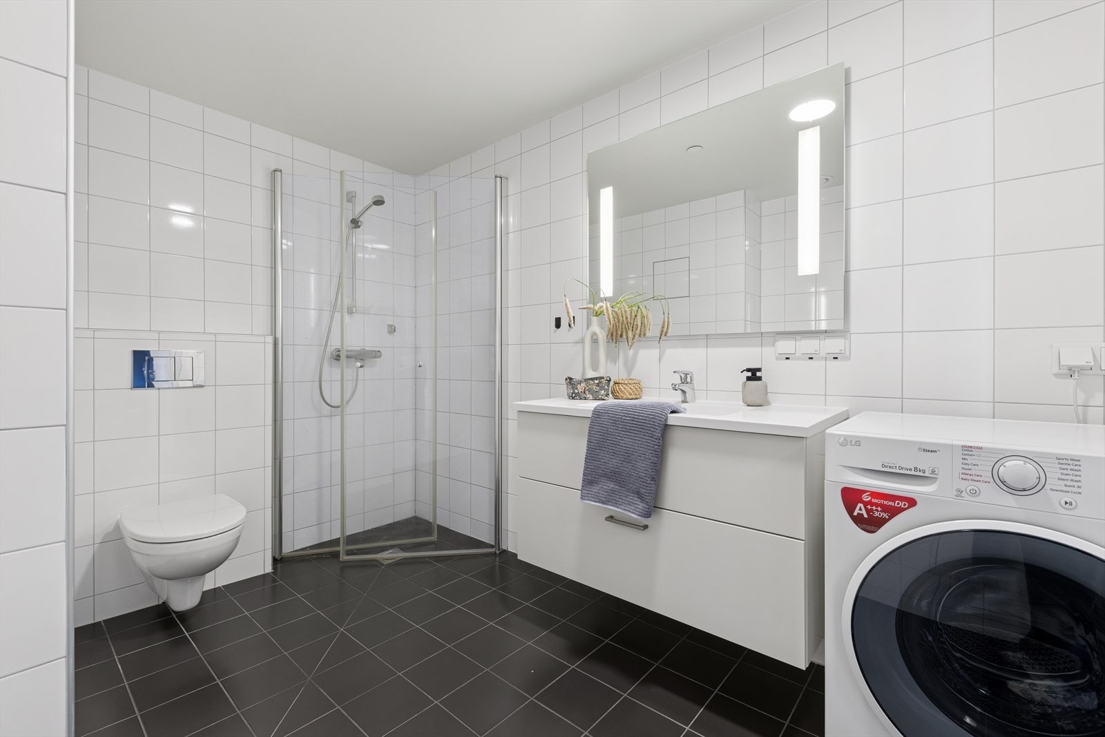 Delikat flislagt bad utstyrt med dusjhjørne, vegghengt toalett og opplegg for vaskemaskin. Det er vannbåre varme i gulv. Galleribilde