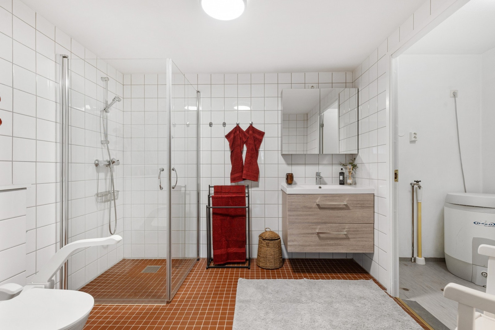 Helfliset bad innredet med dusjhjørne med glassdører, vegghengt toalett, speilskap og servantinnredning med nedsunket servant Galleribilde