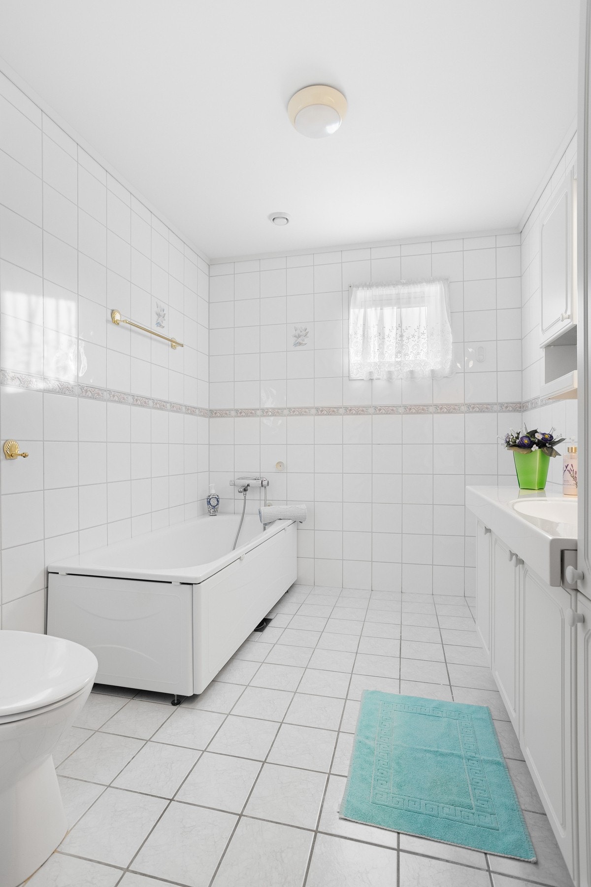 Bad med gulvmontert toalett og badekar. Flislagte vegger og gulv med innredning bestående av speil og underskap Galleribilde