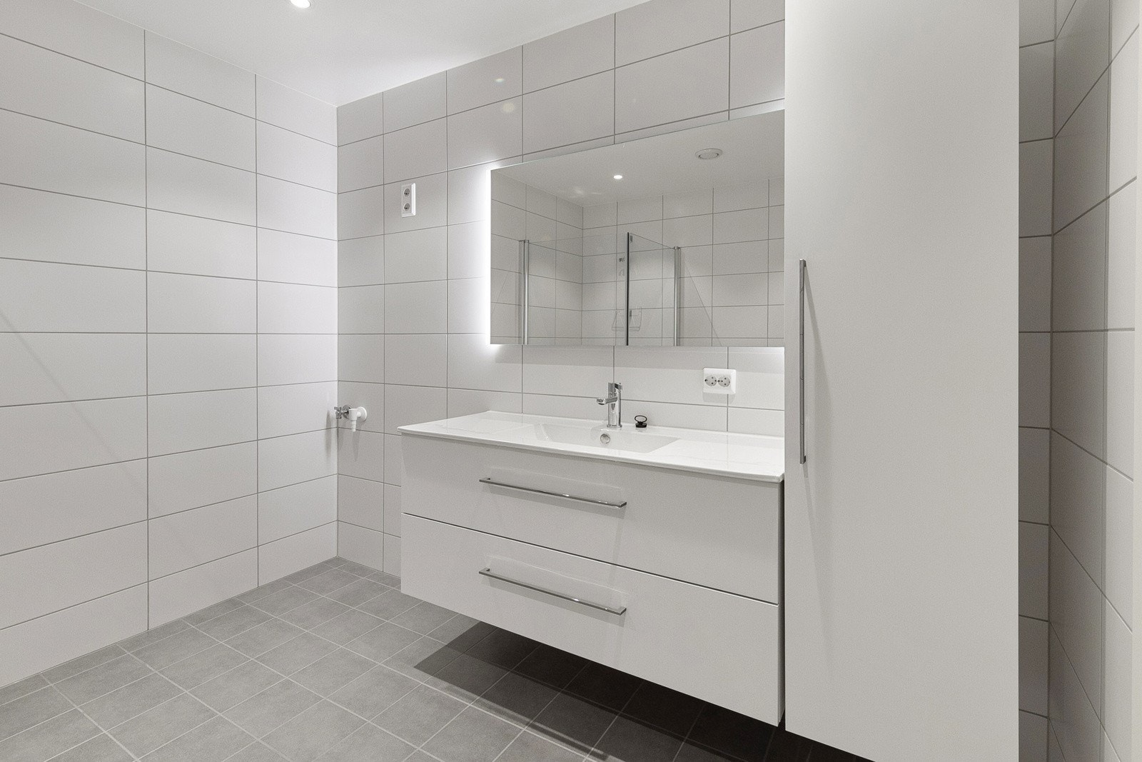 Servant med skuffer, speil med lys og skap til høyre. Opplegg til vaskemaskin og tørketrommel til venstre. Galleribilde