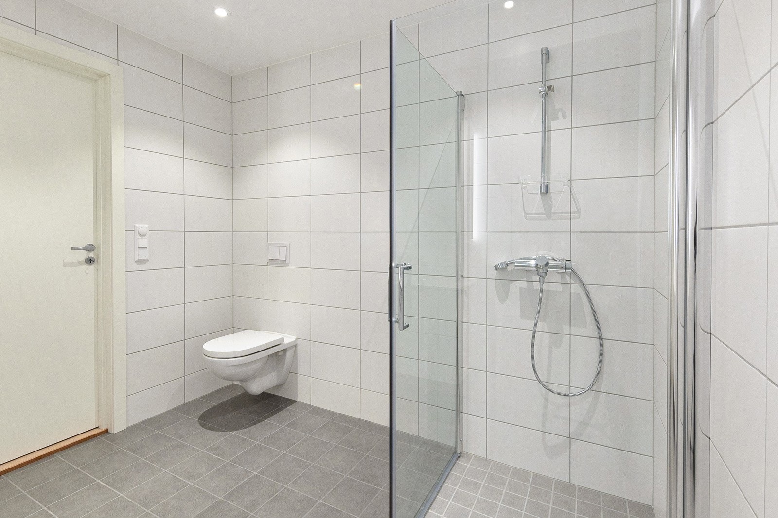 Romslig og stilrent bad med flis og varmekabel på gulv. Vegghengt toalett og dusjhjørne med foldedører slik at man får utnyttet plassen godt. Galleribilde