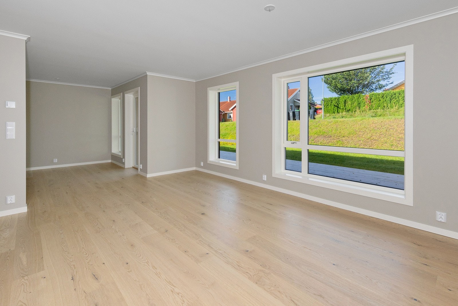 Det er store vinduer som slipper inn rikelig med naturlig lys, og gir utsikt til den grønne hagen utenfor, med gressplen og hekker. Galleribilde