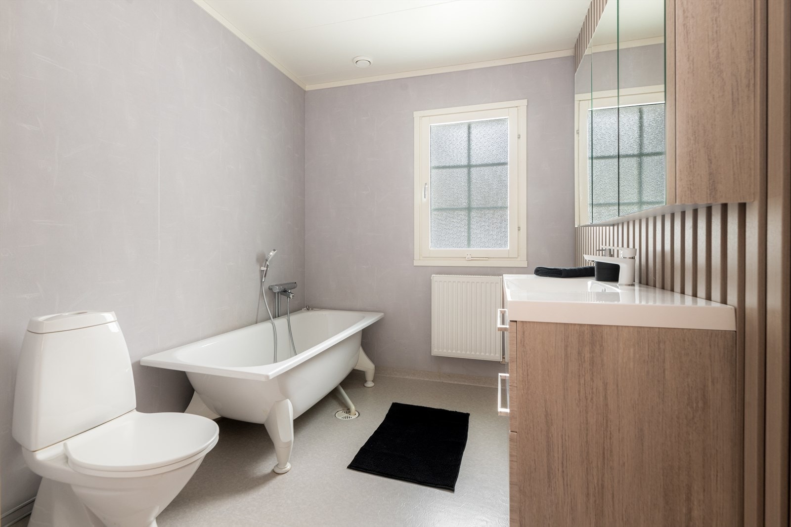 Romslig bad fra byggeår, utstyrt med gulvmontert toalett og badekar med dusjløsning, samt plassbygd høyskap. Galleribilde