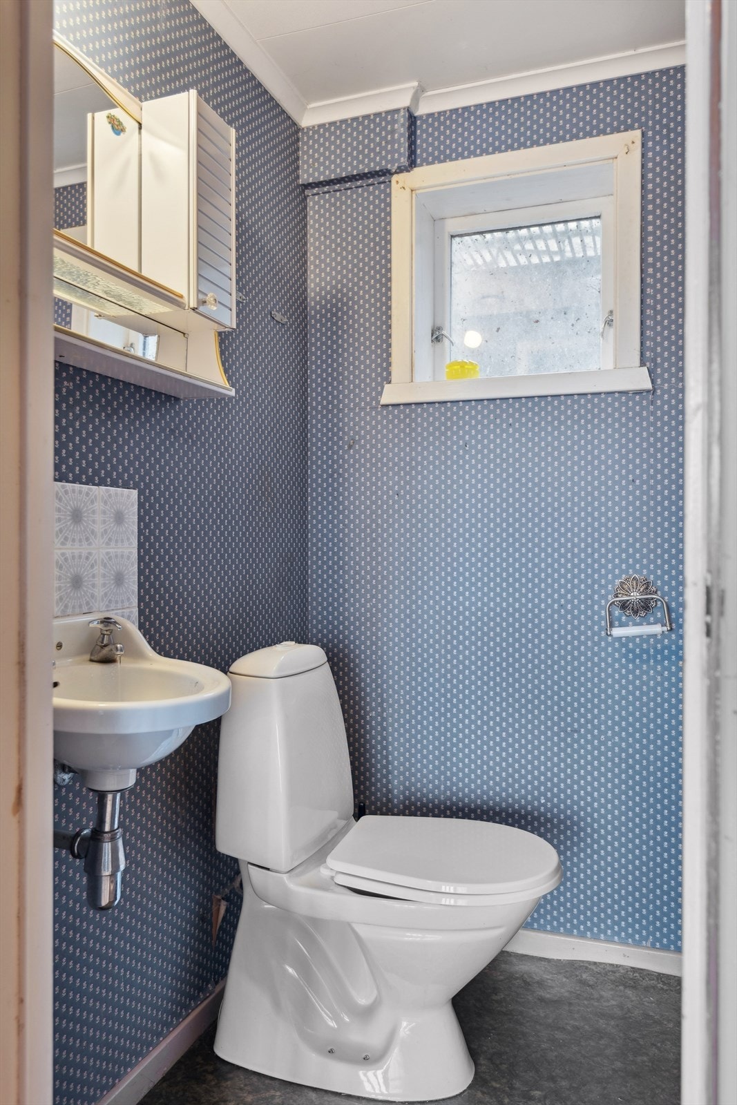 Toalettrom i underetasjen med eldre, gulvmontert toalett og servant på vegg. Rommet har naturlig avtrekk. Galleribilde