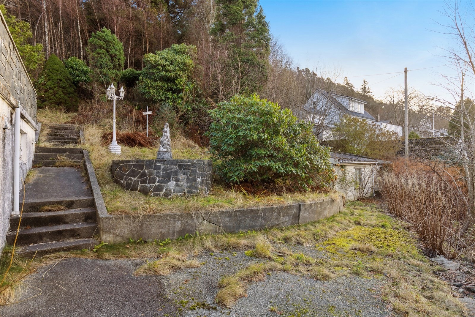 Skrånende eiertomt opparbeidet med asfaltert innkjørsel og gårdsplass, plen, diverse beplantning, forstøtningsmurer/trapper mm. Galleribilde