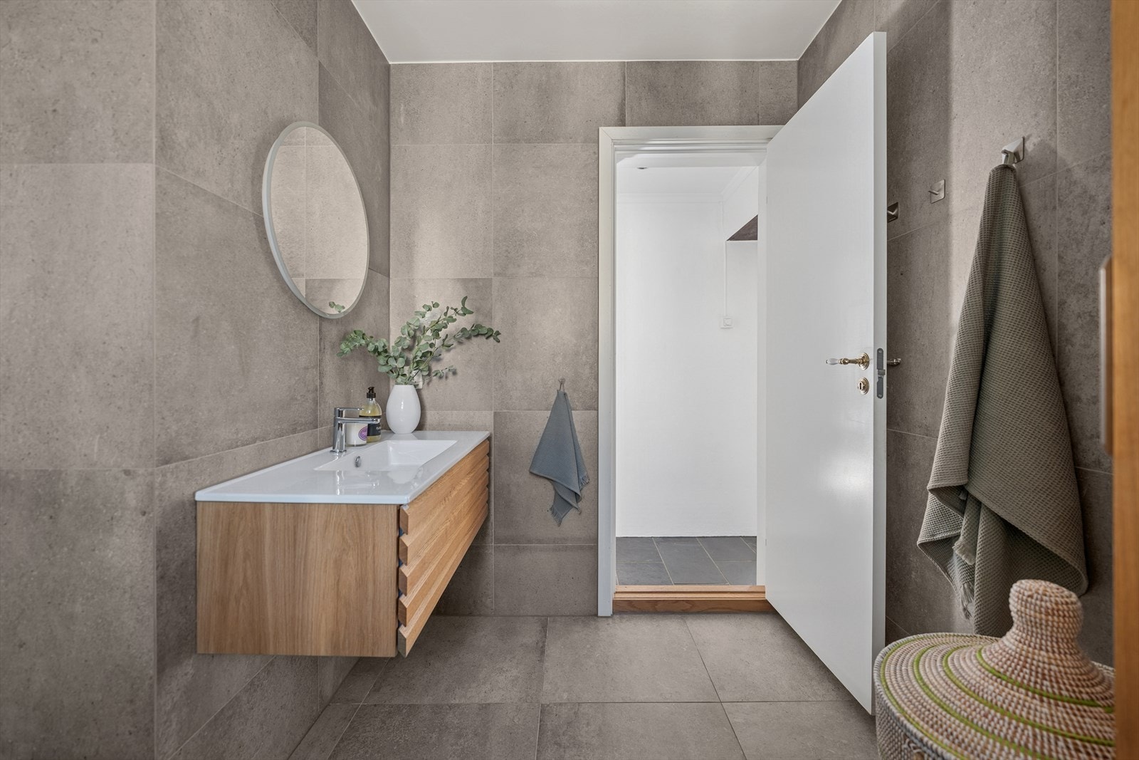 Badet består av svingbare dusjvegger og dusjbatteri i krom med både hånd- og regnfallsdusj, vegghengt servantskap med heldekkende vask, veggmontert speil med touchfunksjon og lys og vegghengt toalett. I tillegg har badet opplegg for vaskemaskin. Galleribilde