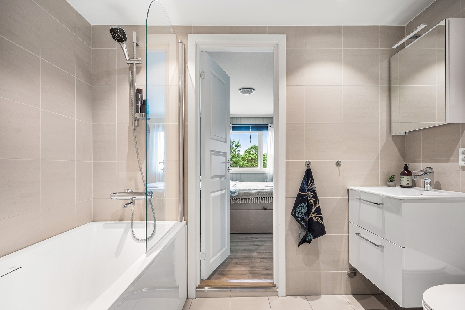 Badet fra 2023 er delikat med flislagte overflater, gulvvarme og downlights. Innredningen består av skuffeseksjon med nedfelt servant, speilskap vegghengt toalett og badekar med dusjmulighet. Galleribilde