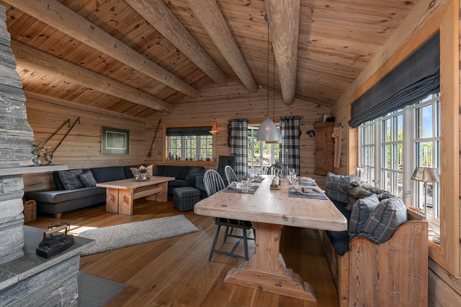 Stue med synlige bjelker, peis og spisebord. Store vinduer gir godt lysinnslipp. Galleribilde