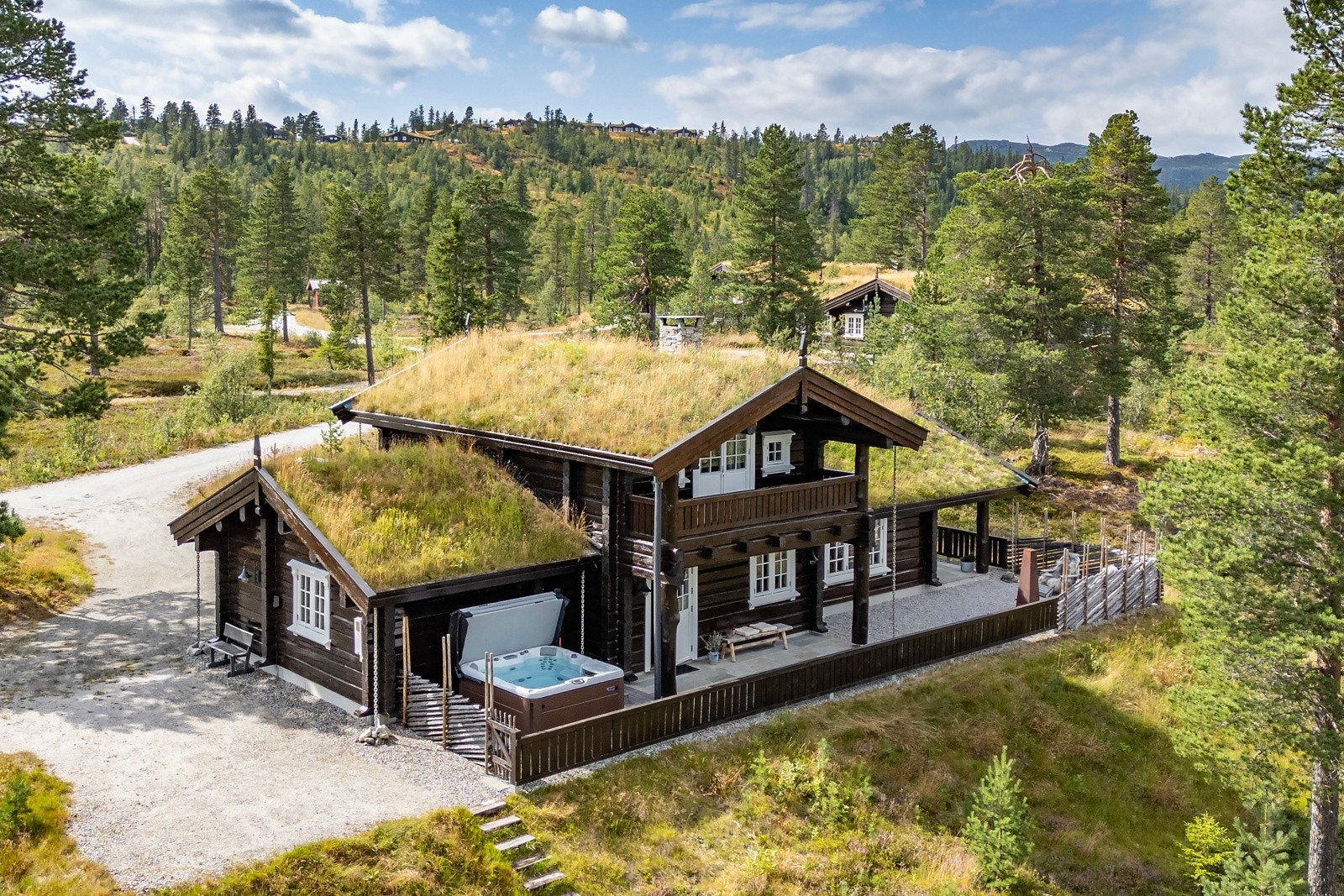 Tradisjonell hytte med torvtak og utendørs boblebad, omringet av skog og fjellandskap. Galleribilde