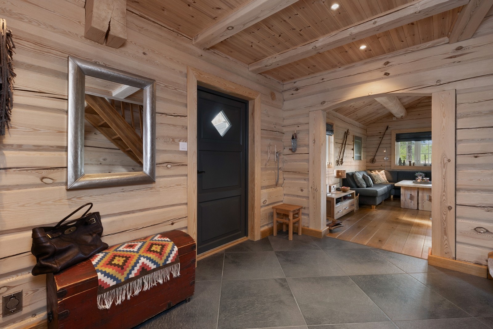 Entré med fliser på gulvet, trevegger og synlige bjelker. Åpen løsning mot stue med sofagruppe. Galleribilde