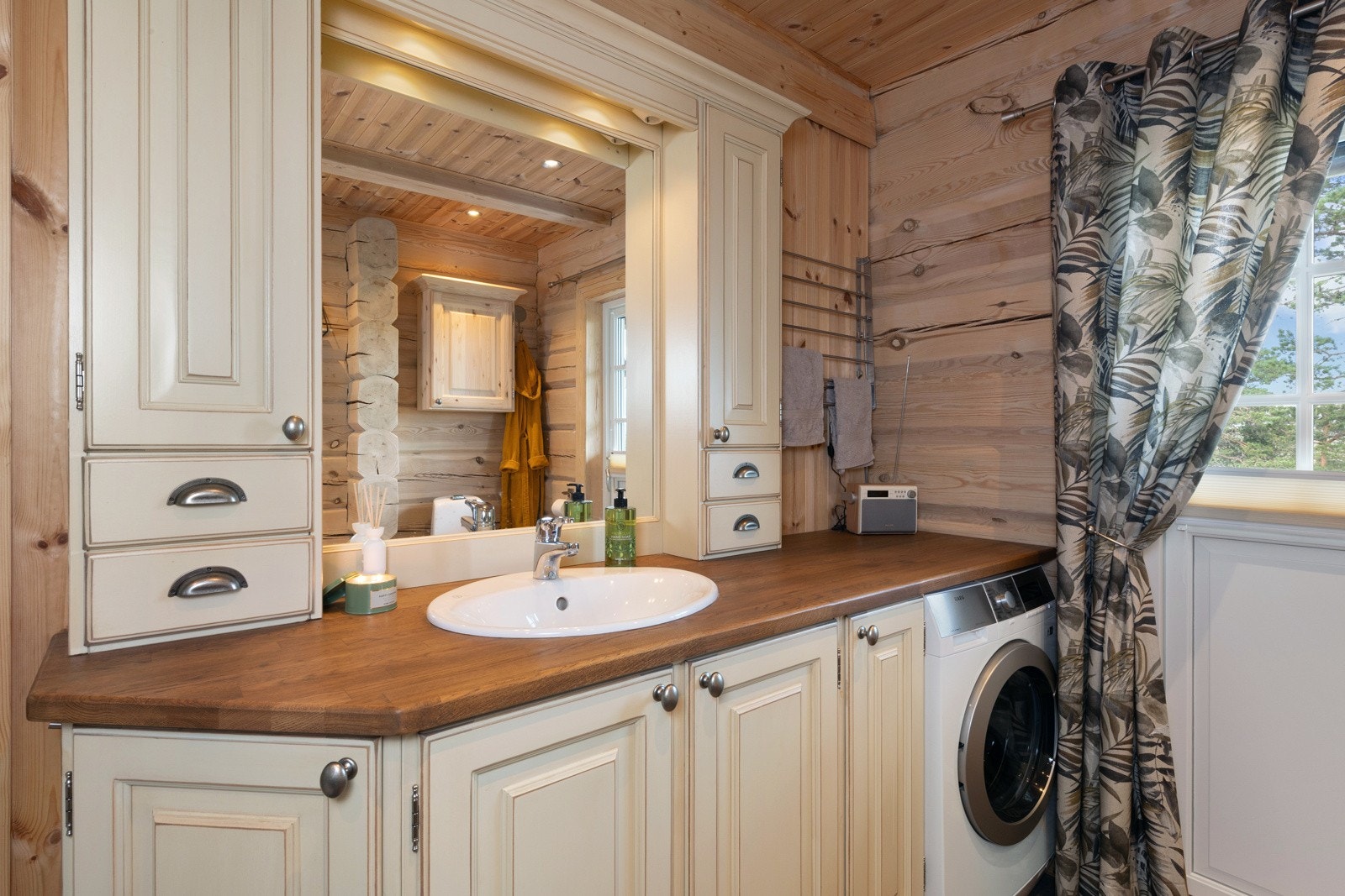 Baderom med opplegg for vaskemaskin, servant og skapinnredning. Vindu i dør som gir naturlig lys. Galleribilde