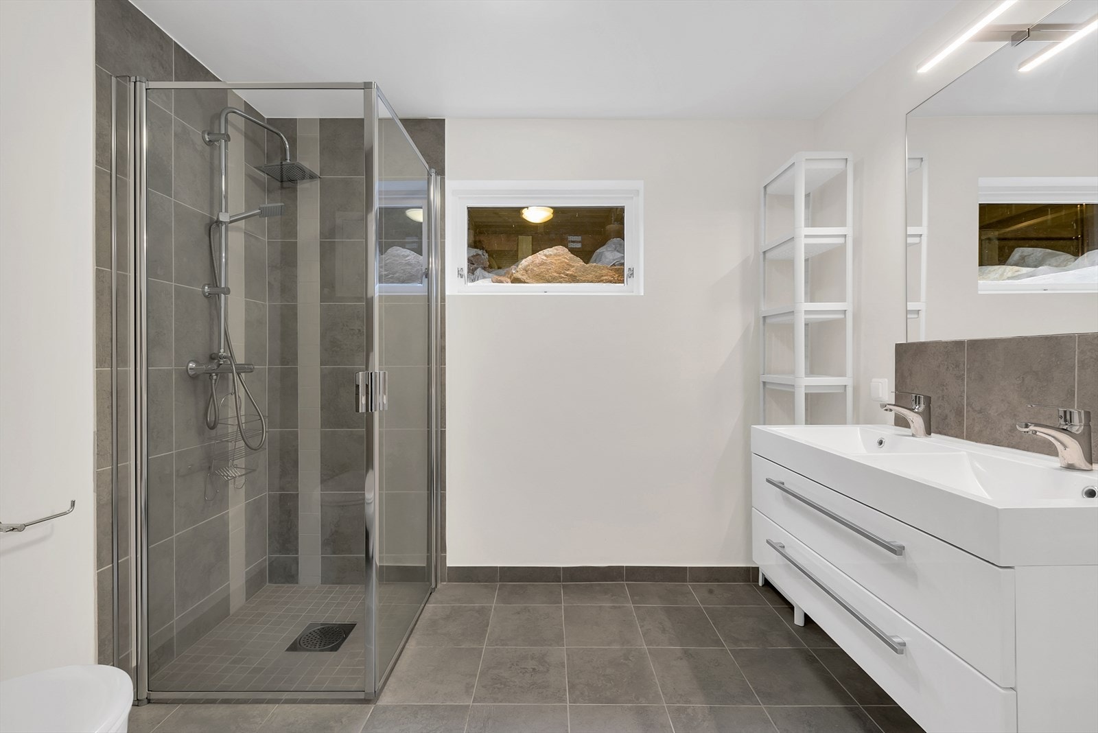 Baderom i underetasjen med innlagte varmekabler. Innredningen består av benkeskap med glatte fronter, to servant, veggfestet klosett med innebygget sisterne og dusjhjørne med dører i herdet glass. Galleribilde