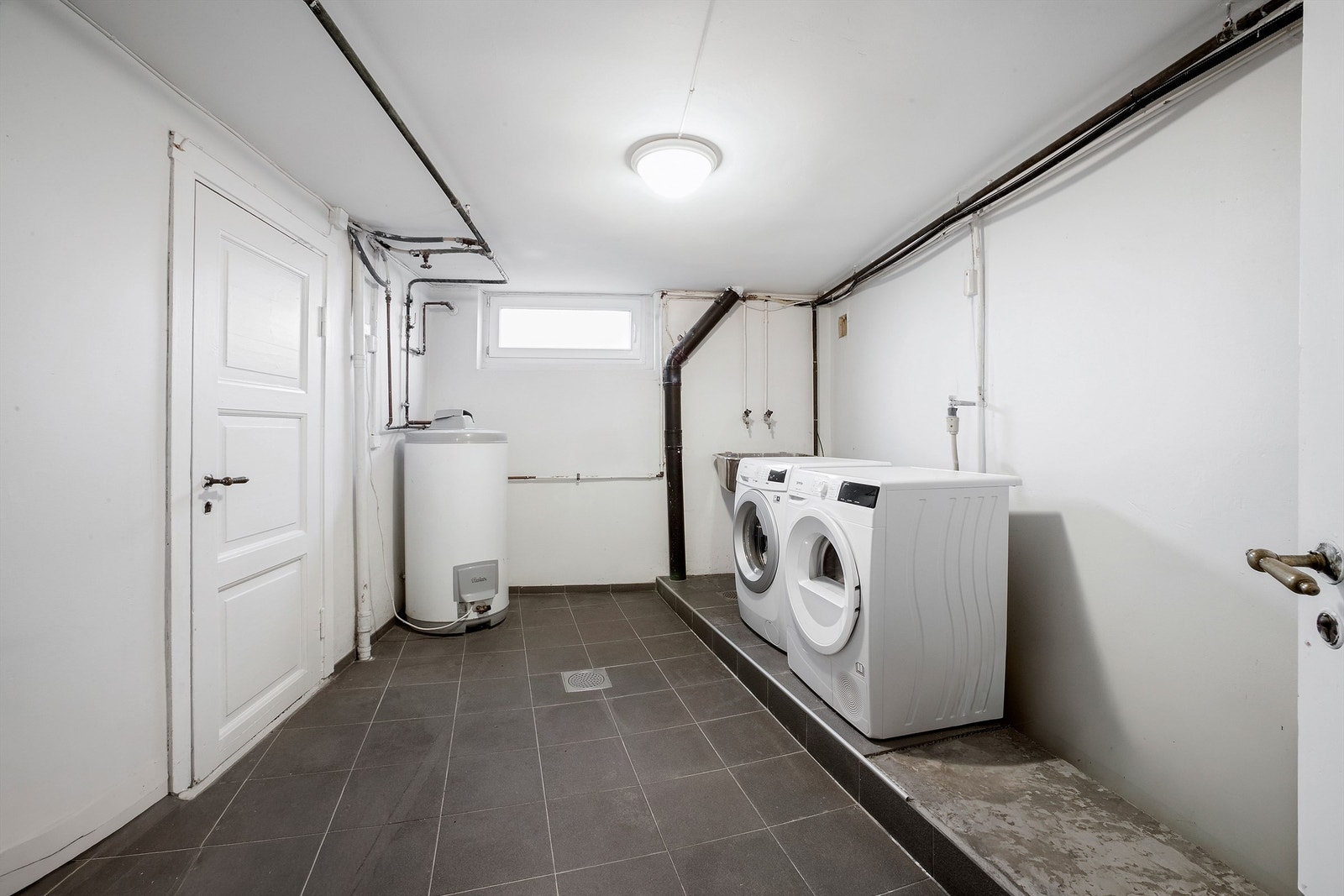 Vaskekjeller med flislagt gulv med nyere pvc-sluk og malte betongvegger Galleribilde