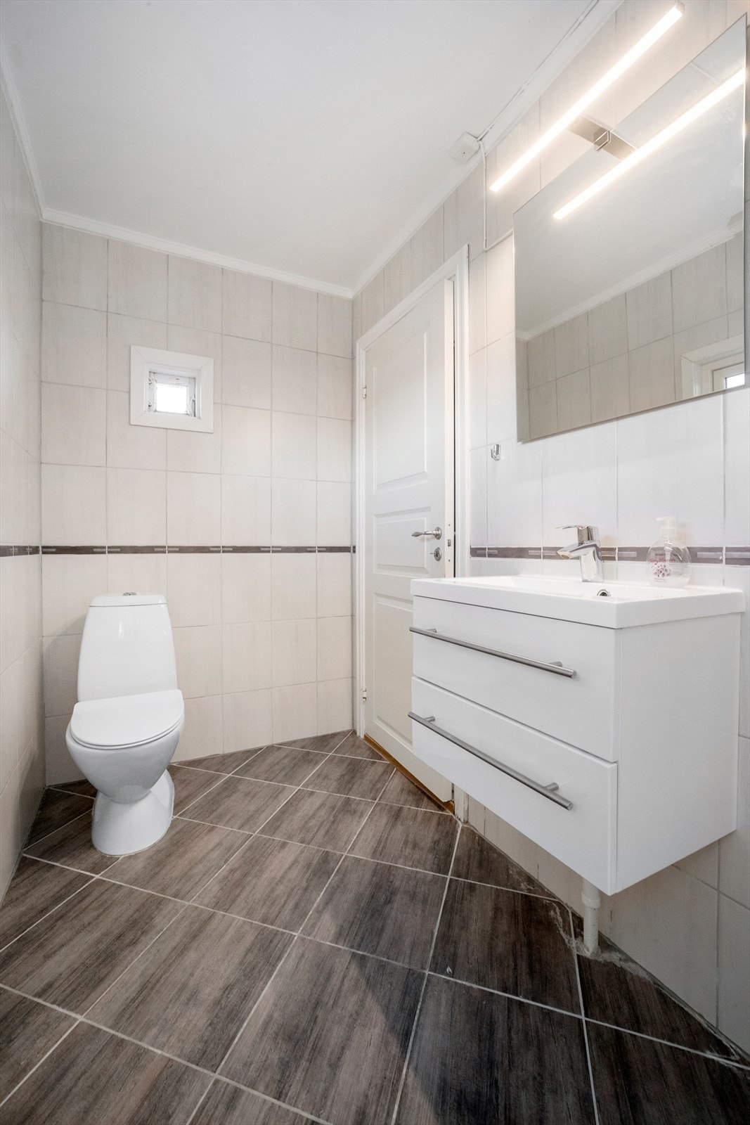 Badet er innredet med gulvstående klosett, vegghengt servantskap med slette fronter og heldekkende servant Galleribilde