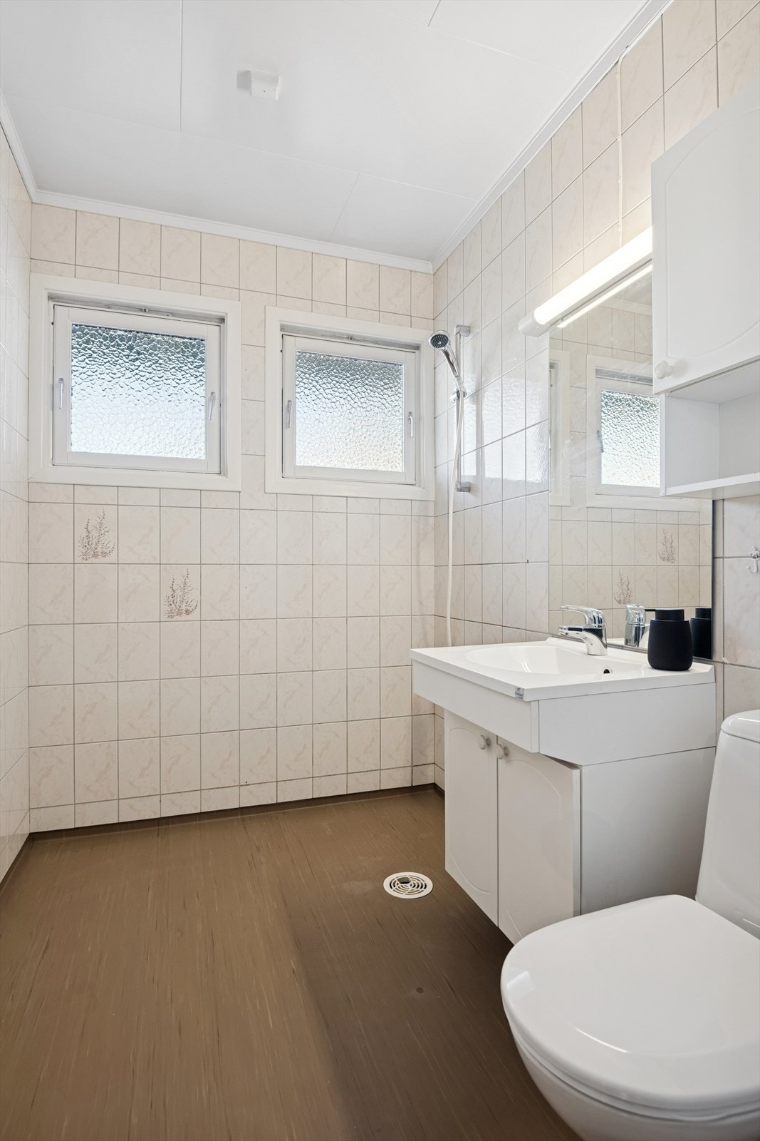 Badet i første etasje har flislagte vegger, vinylbelegg på gulv og dusjhjørne. Galleribilde