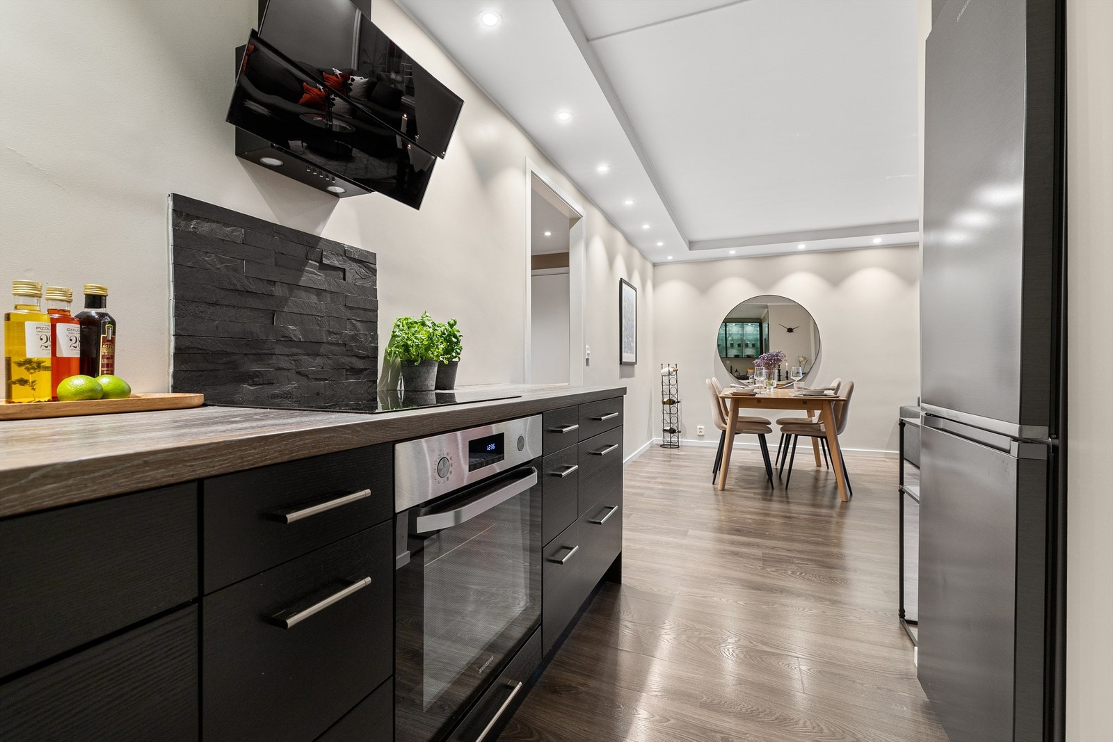 Integrerte hvitevarer som stekeovn, induksjonskoketopp med ventilator over og smal oppvaskmaskin, samt nisje til kjøleskap Galleribilde