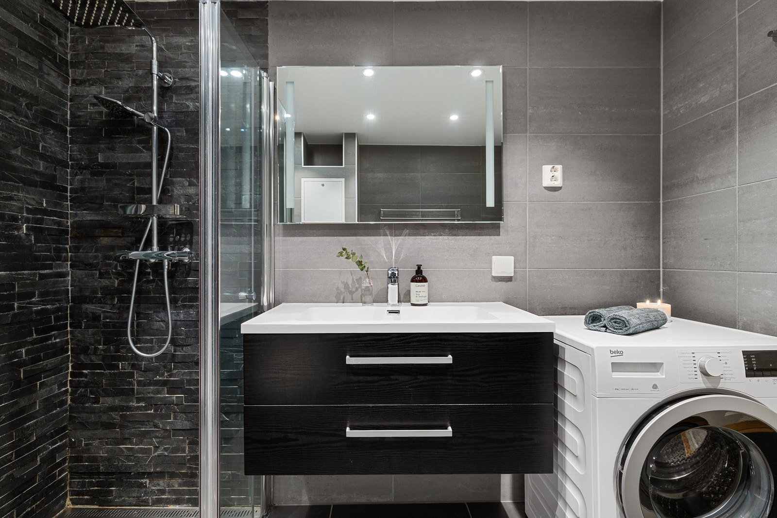 Badet er utstyrt med heldekkende servant med skuffeinnredning, speil med integrert belysning over, vegghengt toalett, samt romslig dusj med innfellbare glassdører og rainshower Galleribilde