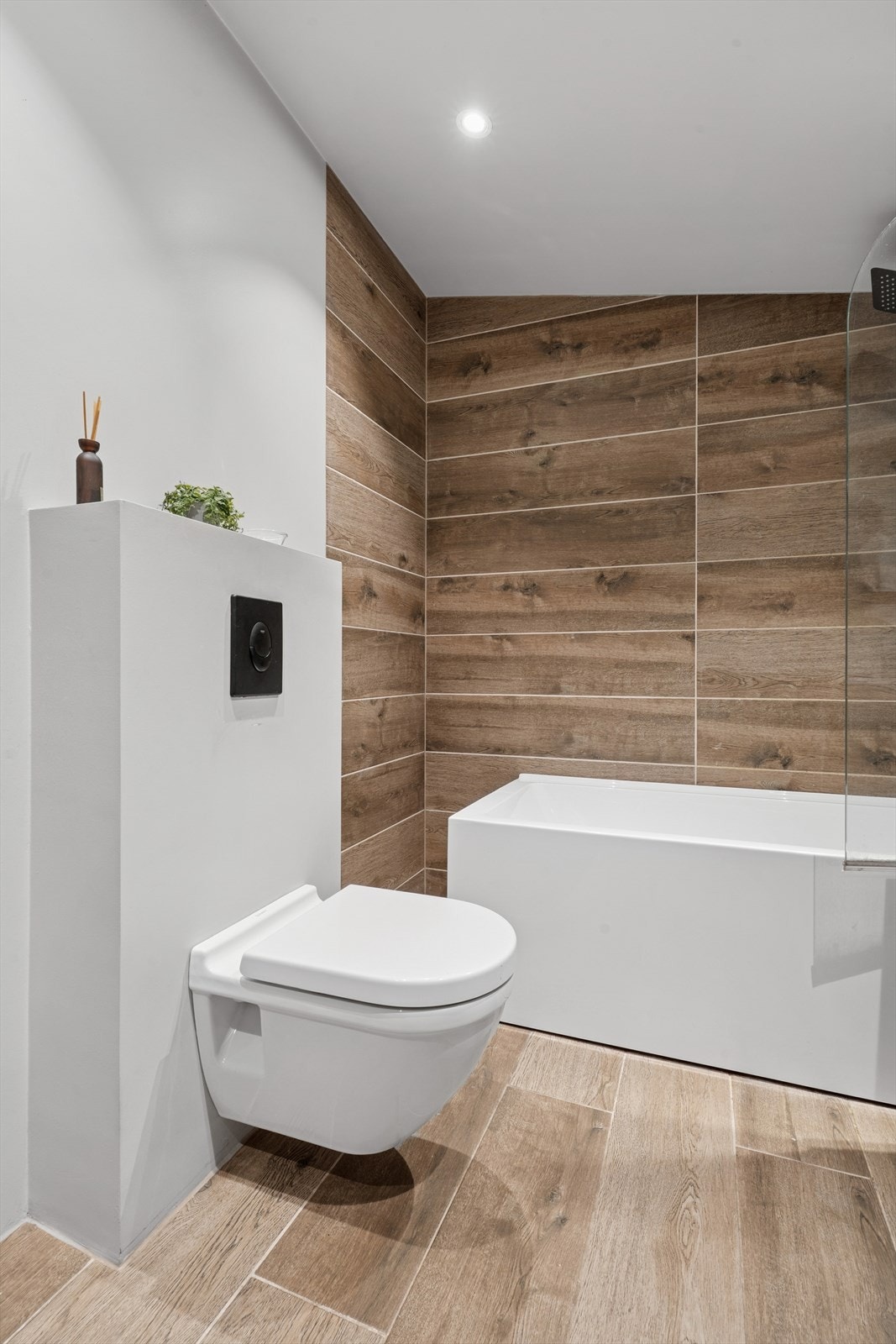 Rommet har fliser i tre-look på gulv og i dusjsonen, samt et moderne vegghengt toalett. Galleribilde