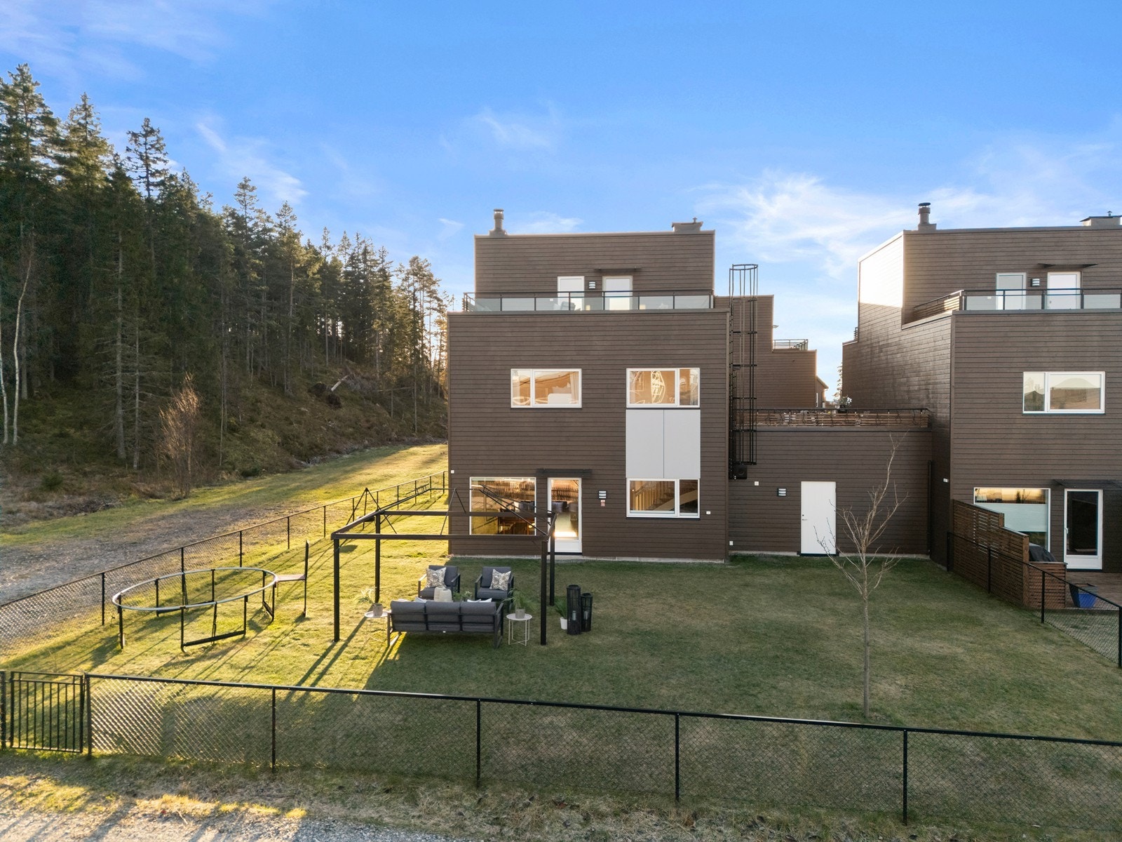 Et moderne kjedehus fra 2022 med en romslig, inngjerdet hage, grensende mot skogkanten innerst på tunet. Galleribilde