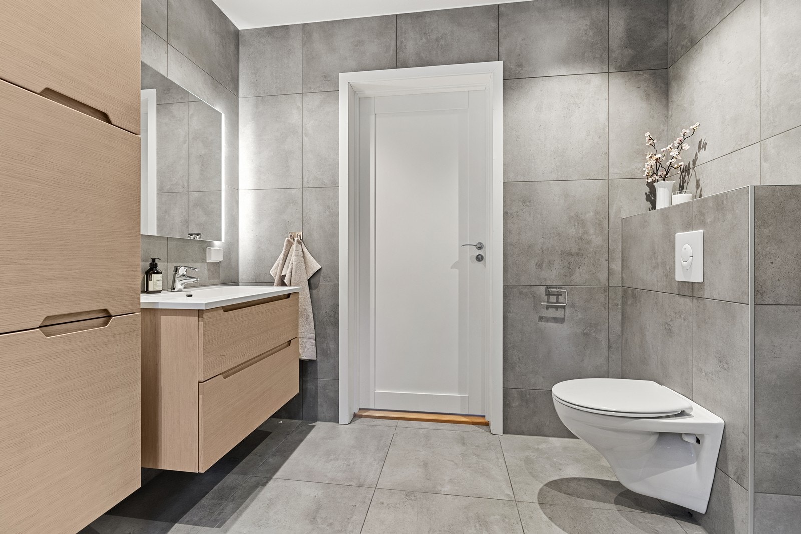 Badet er utstyrt med vegghengt toalett, servant med skuffer, badekar og dusjnisje med innfellbare glassdører. Galleribilde