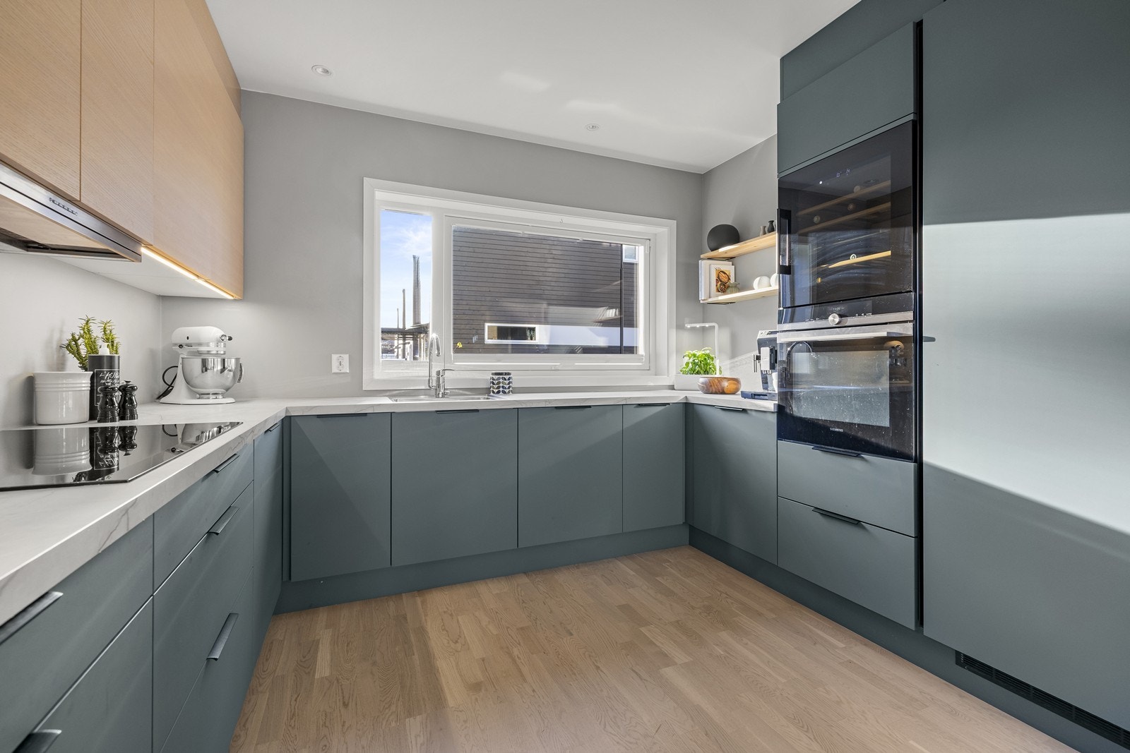 Integrerte hvitevarer som koketopp, stekeovn og vinskap i ståhøyde, oppvaskmaskin og kjøle-/fryseskap. Galleribilde