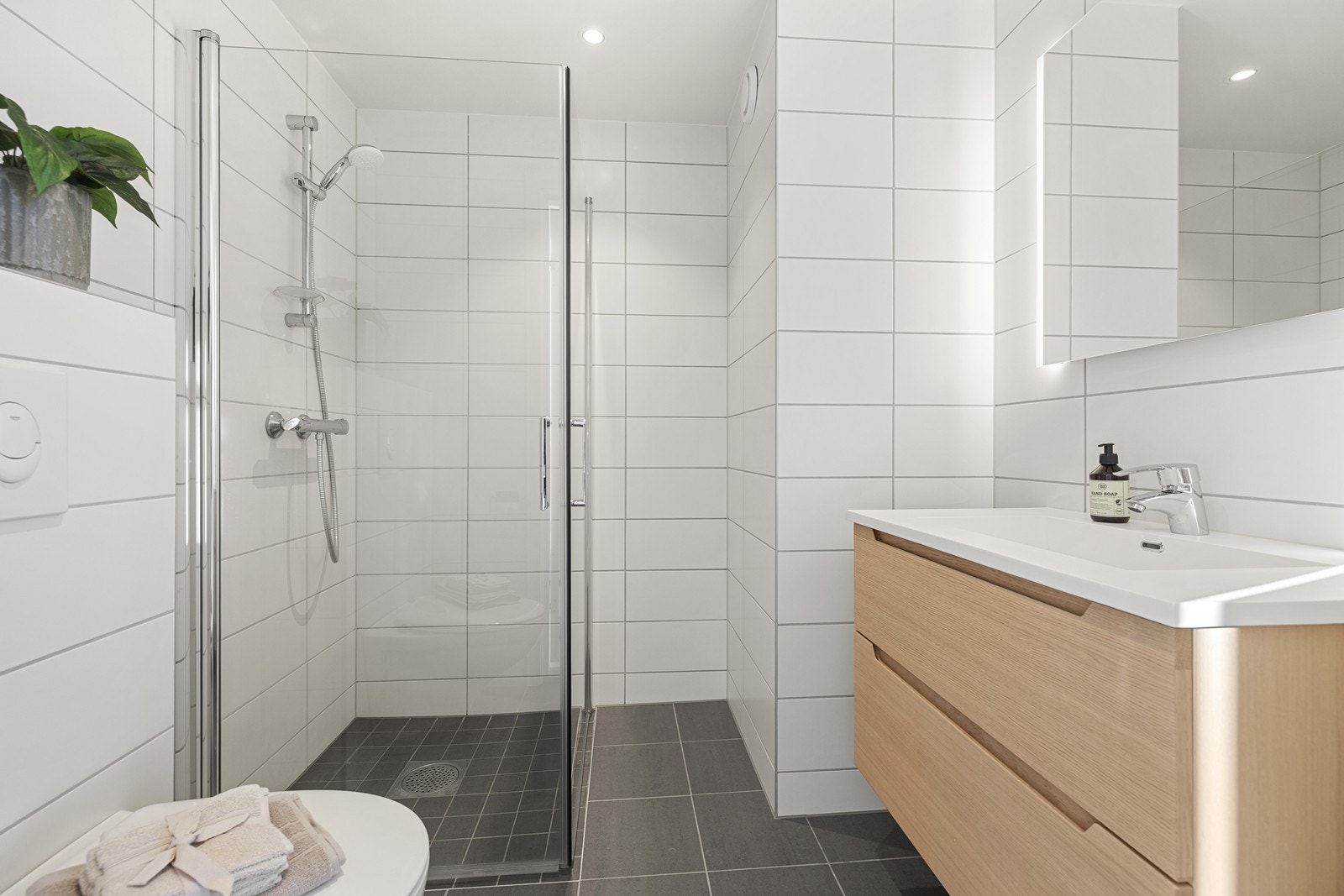 Pent flislagt bad i tidløse fargetoner. Badet innehar vegghengt toalett, servant med skuffer og dusjnisje med innfellbare glassdører. Galleribilde