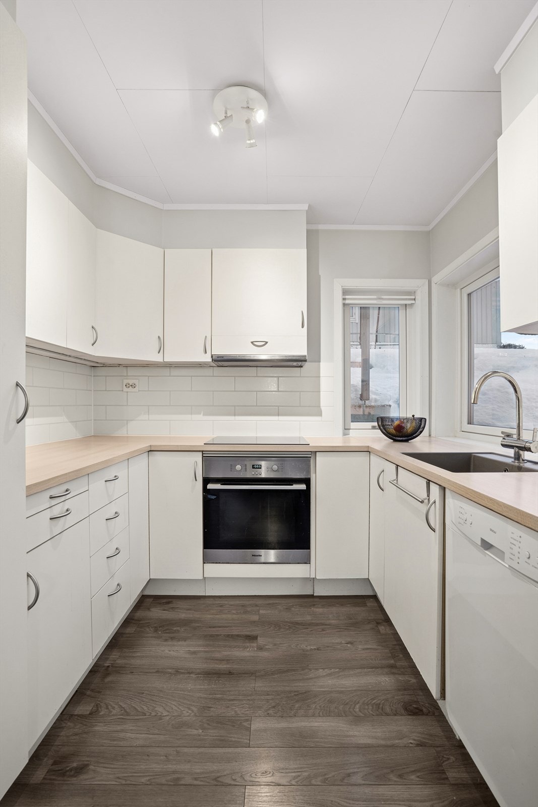 Kjøkken har mye skapplass, hvite slette fronter og rikelig med naturlig lys fra store vindusflater Galleribilde