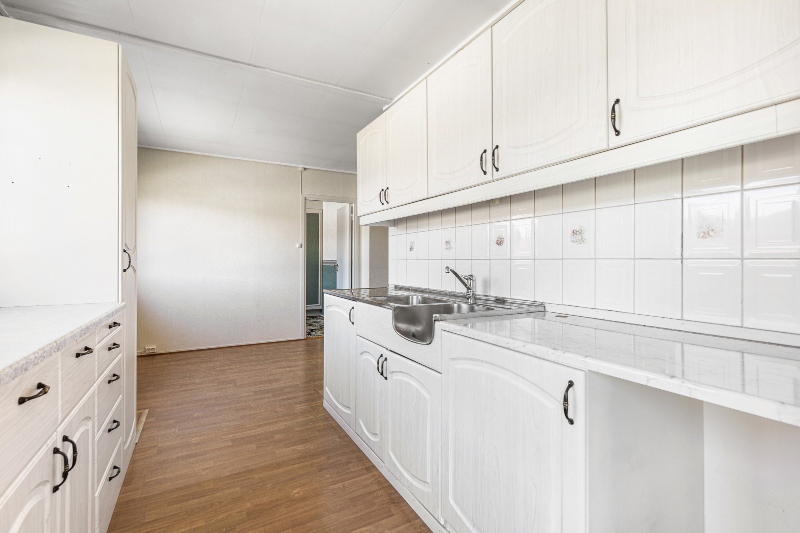 Lyst kjøkken med hvite skap, hvite fliser og parkettgulv. Galleribilde