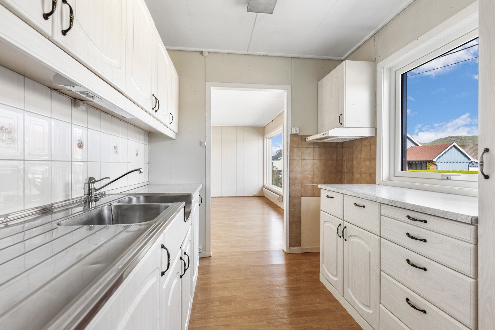 Kjøkken med lyse skapfronter, dobbel vask og vindu som gir godt lysinnslipp. Adkomst til stue med parkettgulv. Galleribilde