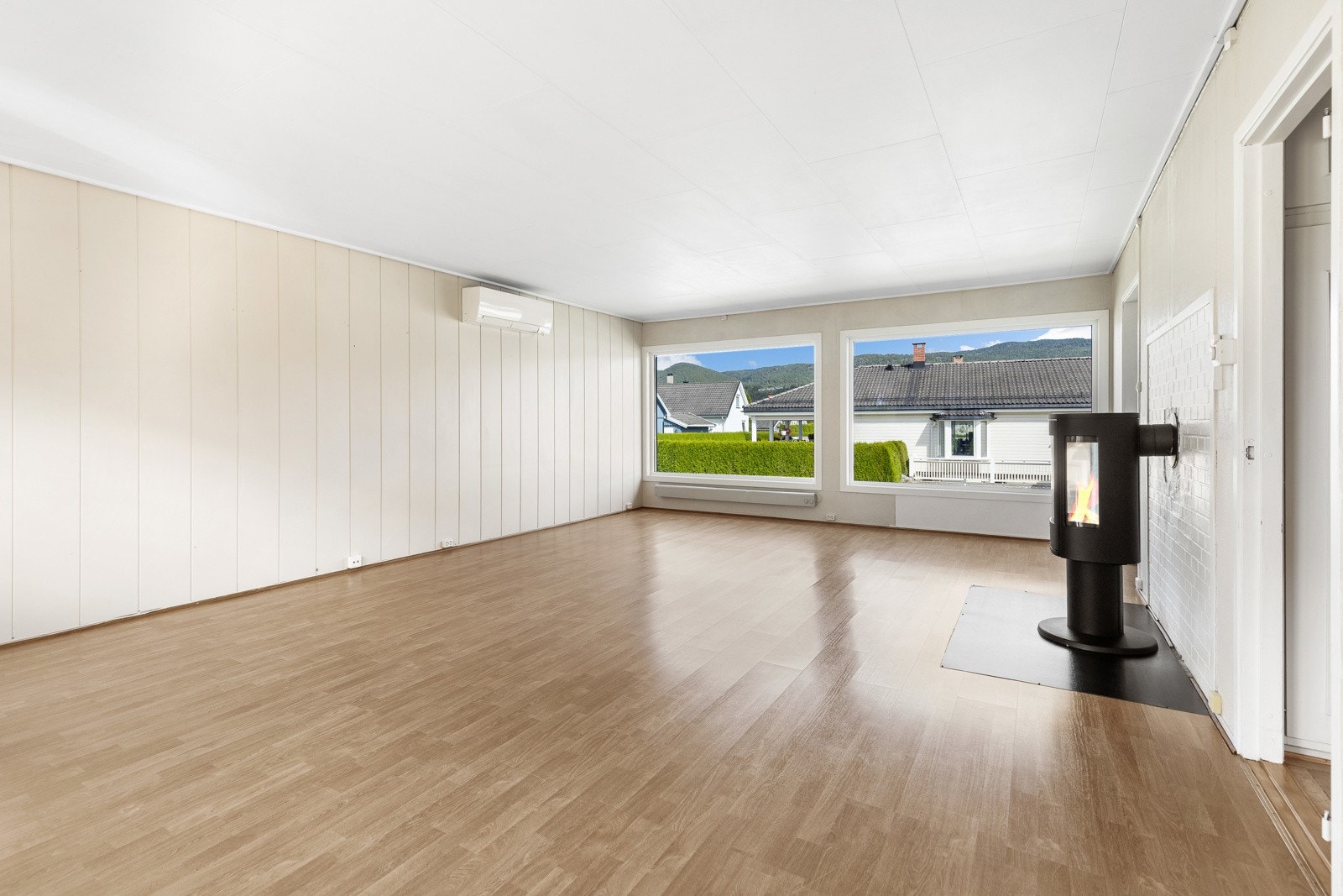 Romslig stue med store vinduer, peisovn og lysmalte vegger. Galleribilde