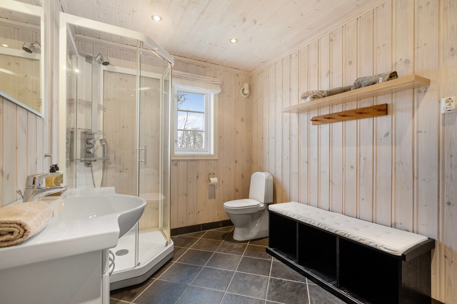 Badet er fra byggeår og har flislagt gulv med varmekabler og panelerte vegger som gir en varm og tradisjonell hyttestil Galleribilde