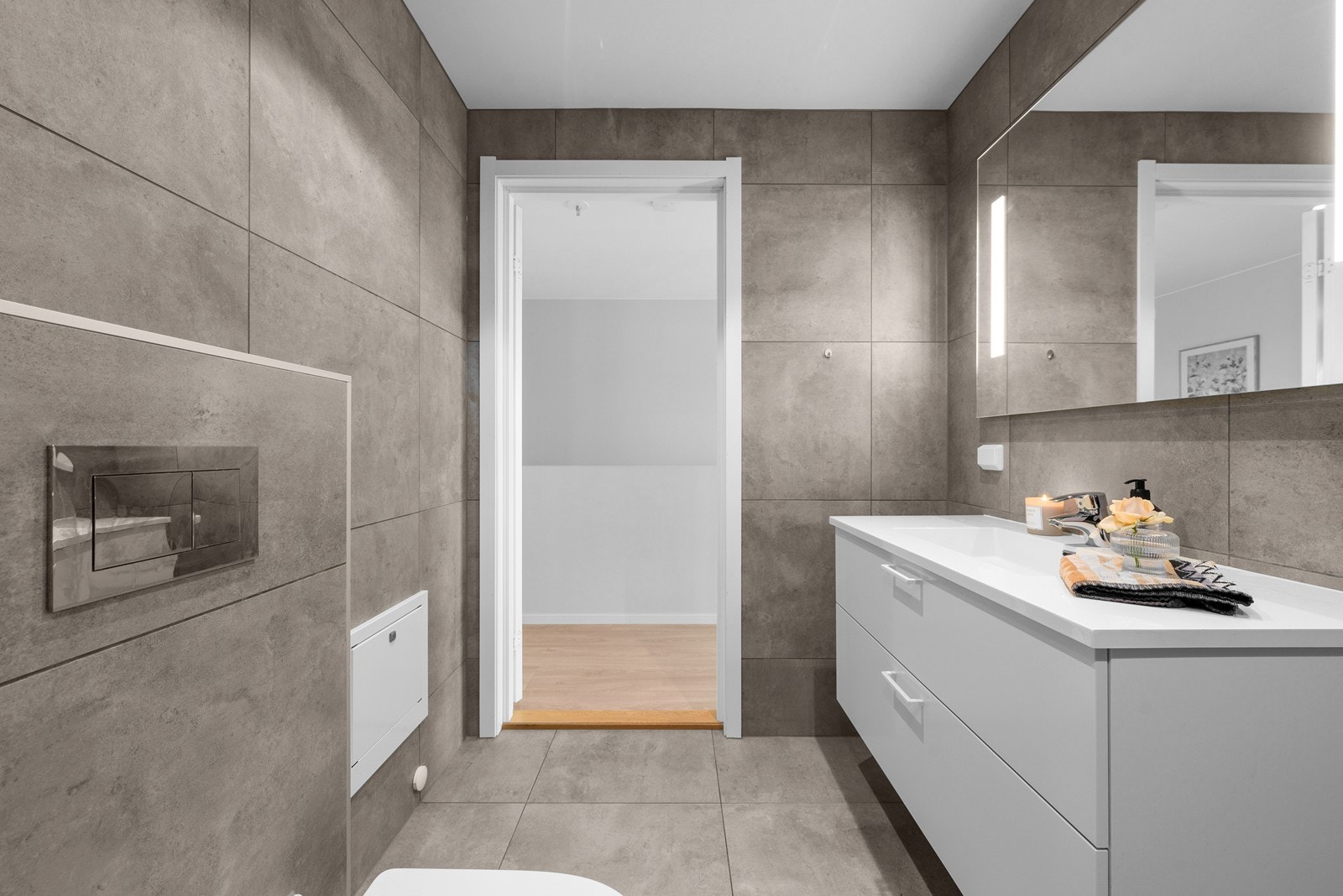 Badet har vegghengt toalett og store, tidsriktige fliser på gulv og vegger. Galleribilde