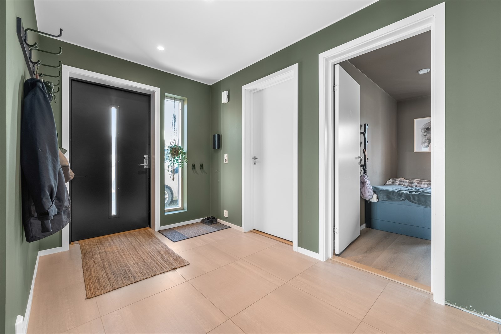 Entreen får dagslys fra ytterdørens glassfelt og har fliser på gulvet. Galleribilde