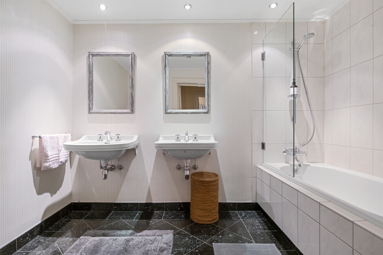 Badet er lyst og moderne, med svarte gulvfliser og en beige flislagt vegg rundt badekaret, avskjermet med en glassvegg. Galleribilde