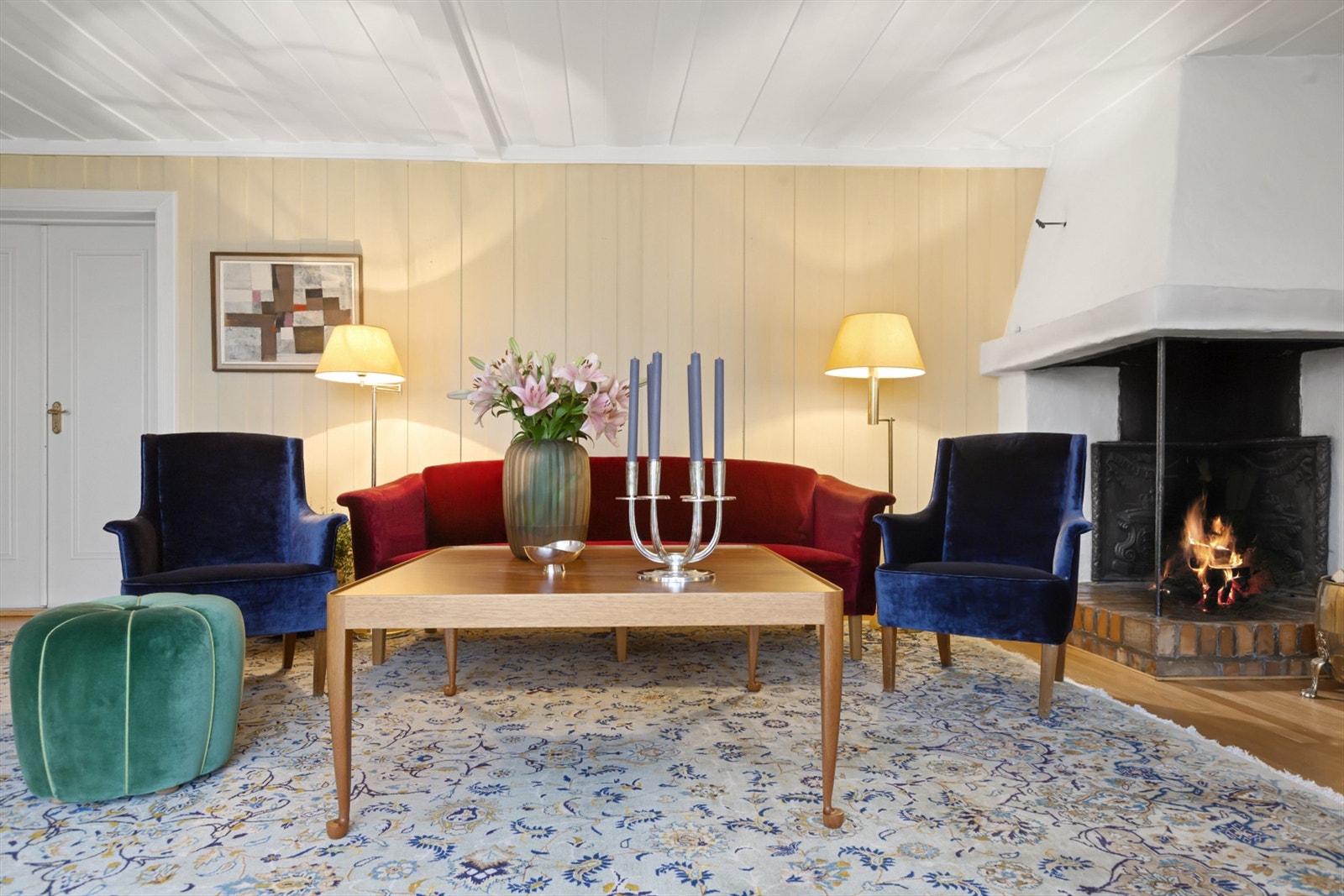 En stor og herskapelig stue med veggpaneler i lyse fargetoner og vedpeis som gir godt med varme. Galleribilde