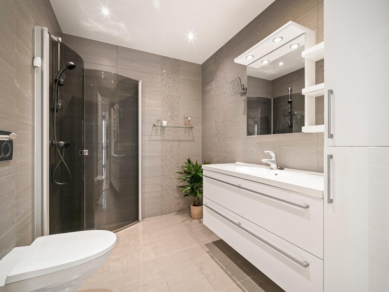 Badet fremstår moderne og stilrent med flislagte vegger og gulv, tak med downlights og gulv med vannbåren gulvvarme. Galleribilde