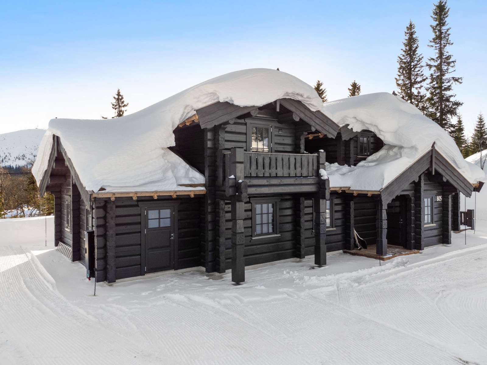 Hytta viser tydelig håndverkskvalitet gjennom laft, torvtak og utsmykkede detaljer. Balkongen i andre etasje gir ekstra nærhet til fjellnaturen og utsikt over området. Galleribilde