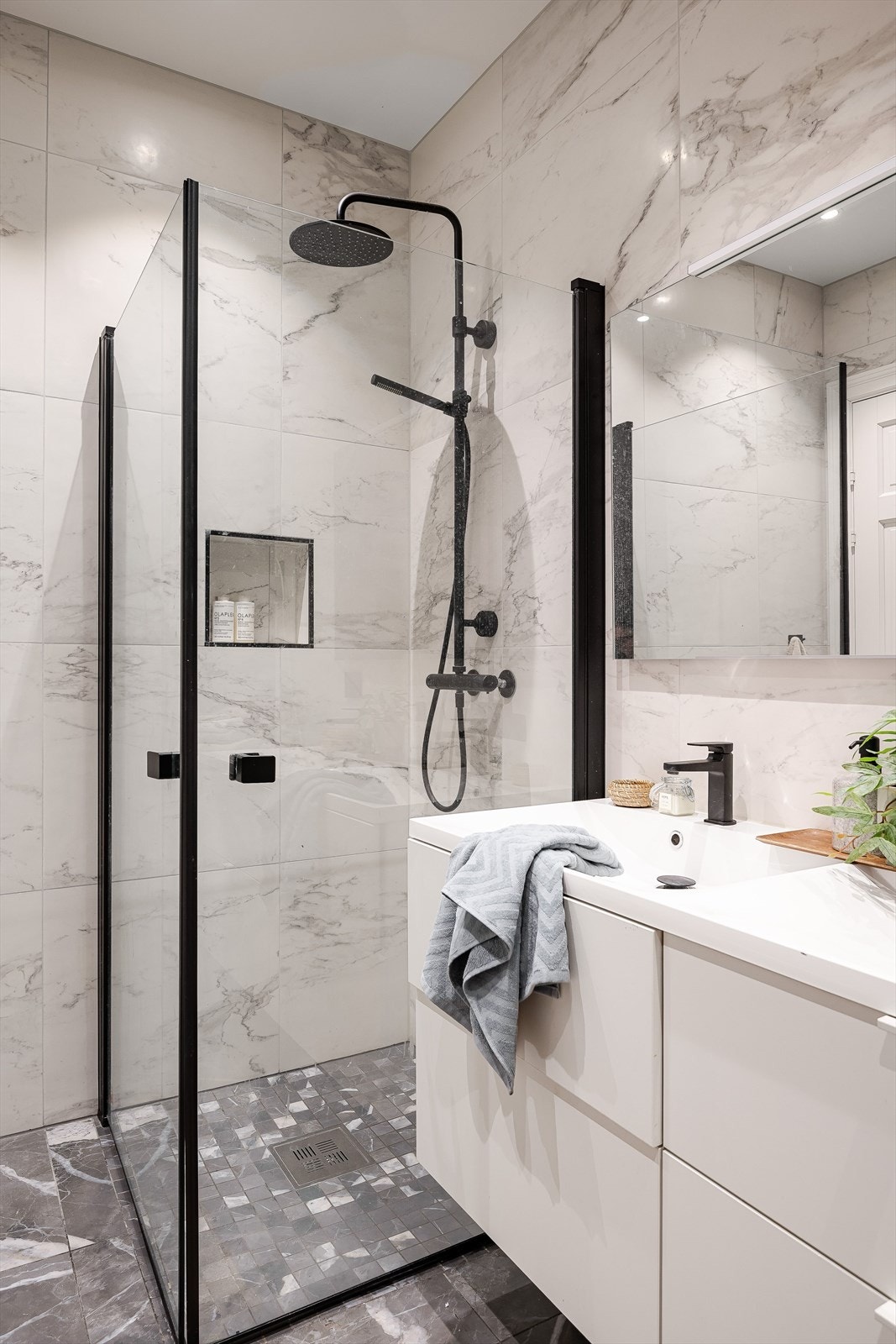 Dusjhjørne med innfellbare dusjdører og vegghengt dusjbatteri med regnfall. Legg merke til den praktiske hyllen i dusjen. Det er elektrisk gulvvarme på badet. Galleribilde