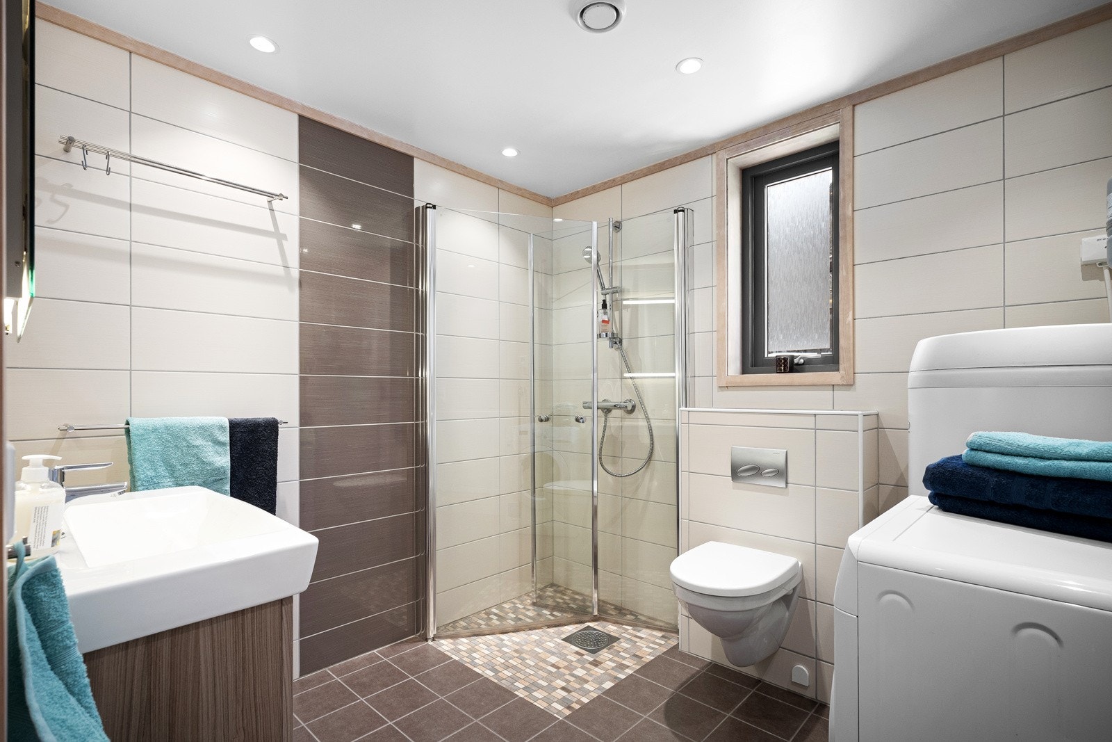 Fint helfliset bad innredet med vegghengt toalett, servant med skuffeseksjon og dusjhjørne med glassdører. Galleribilde