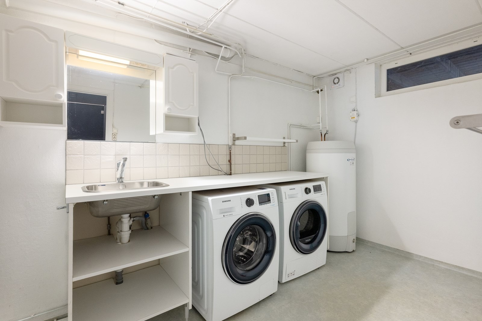 Boligen har et praktisk innredet vaskerom i kjelleren, med god skap- og benkplass og nedfelt vaskekum. Her er plassen godt utnyttet med vaskemaskin og tørketrommel plassert under benkeplata. Vv-tank 2015. Galleribilde