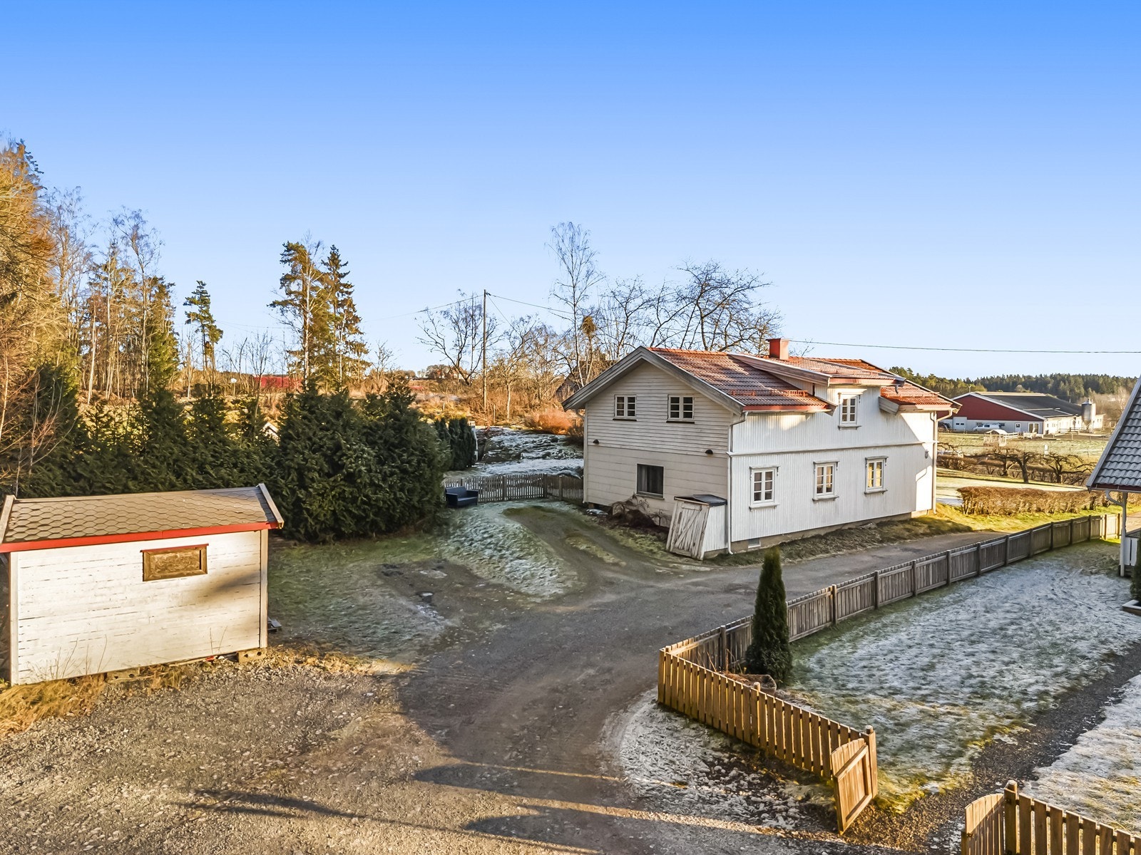 Eiendommen har en gruset gårdsplass og lett skrånende tomt med gressplen og noe beplantning. Galleribilde