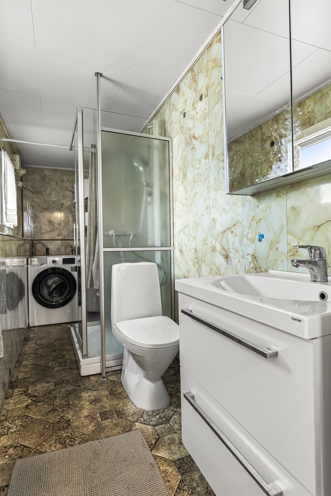 Baderomsplater på veggene og elektriske varmekabler i gulvet gir en praktisk våtromsløsning. Dusjkabinett og opplegg for vaskemaskin kompletterer funksjonaliteten på badet. Galleribilde