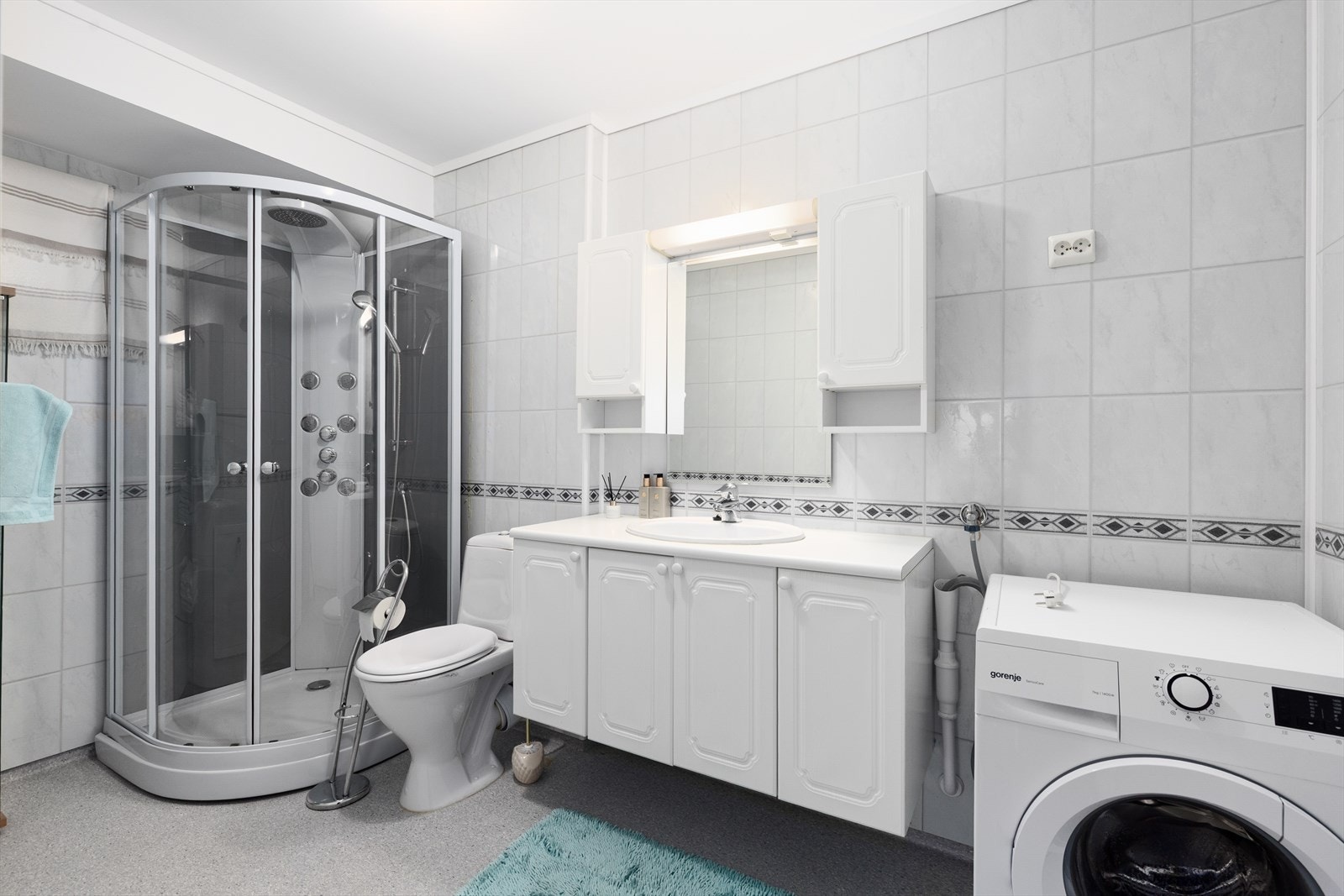 Romslig bad innredet med toalett, dusjkabinett og servantinnredning med skap og speil med overlys. Det er opplegg for vaskemaskin. Galleribilde