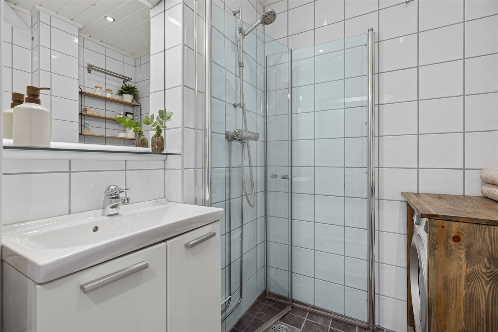 Bad med komplett innredning: WC, servant med underskap, speil med overlys, dusjdører og opplegg for vaskemaskin. Galleribilde