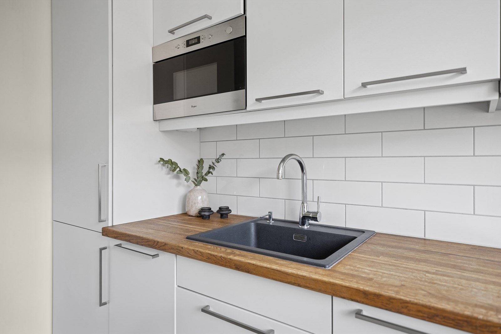 Kjøkken med gjennomført design: glatte fronter, underlys, fliser over benk og heltre benkeplate med kum. Galleribilde