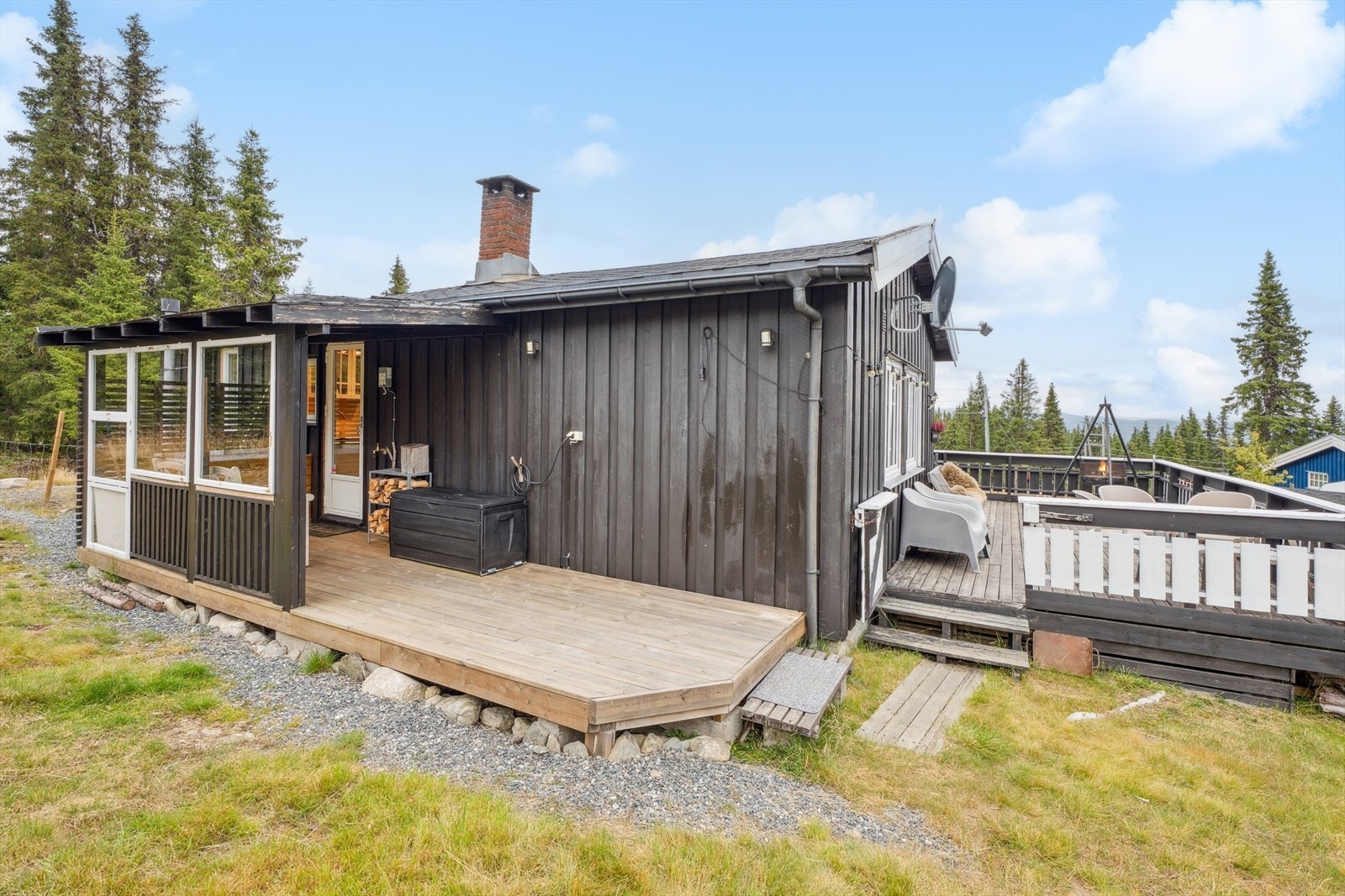 Terrasse på baksiden av hytta, delvis overbygget. På vegg ved verandadør er hentepunktet for vannet. Galleribilde