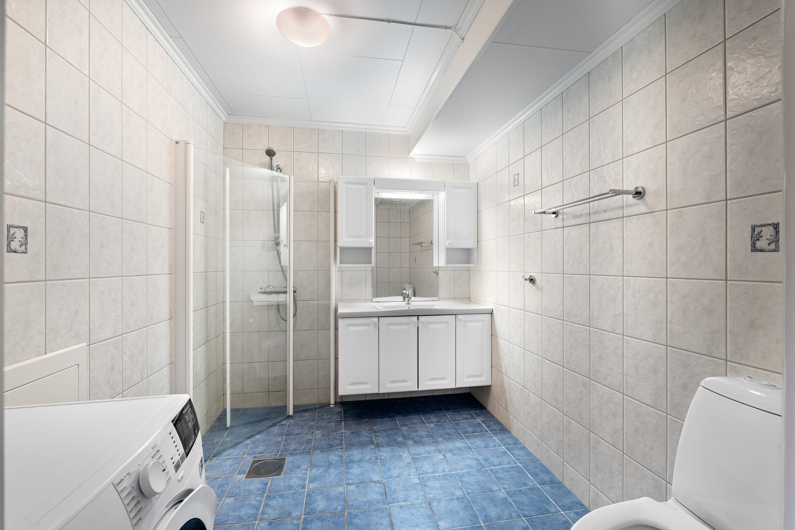 Flislagt bad med varme i gulvet, dusjhjørne med innfellbare glassdører og opplegg for vaskemaskin. Galleribilde