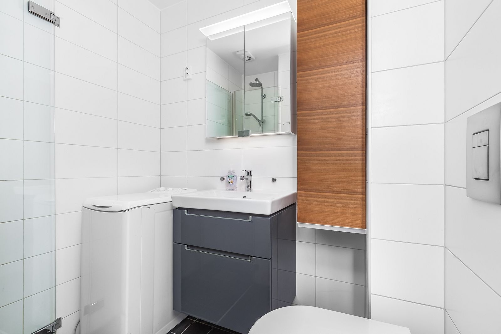 Pent flislagt bad med regnfallsdusj i hjørnet, vaskemaskin inkludert og mye skapplass. Galleribilde