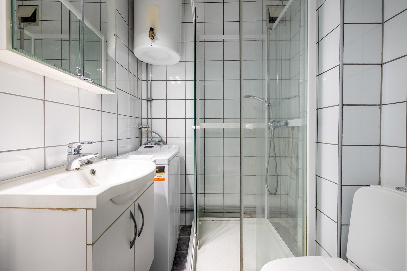 Leiligheten har et flislagt bad med dusjkabinett og toalett - Videre har badet opplegg for vaskemaskin Galleribilde